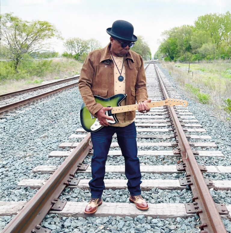 Tito Jackson with guitar on train tracks